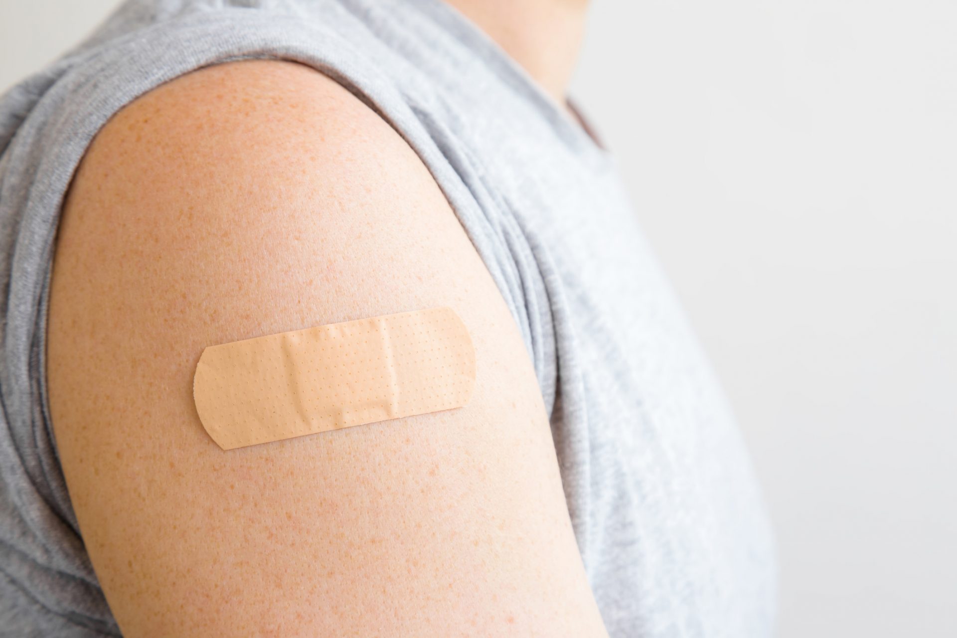 Brown adhesive bandage on young man's arm after scratch on skin or injection of vaccine. First aid. Medical, pharmacy and healthcare concept. Closeup.
